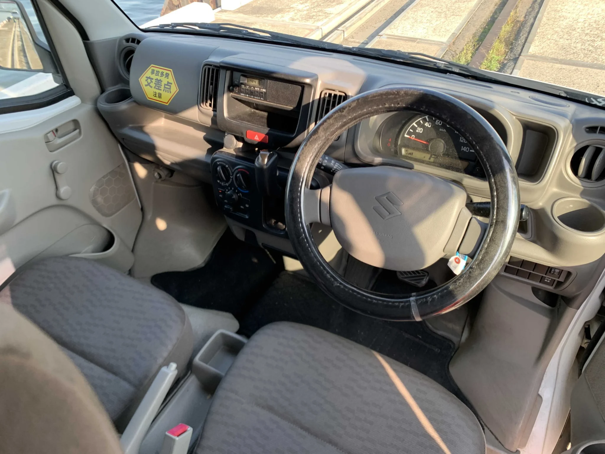 Functional driver cabin layout of the 2020 Suzuki Every highlighting the high-mounted semi-automatic gear lever, basic dashboard cluster, and the driver side single power window master switch.