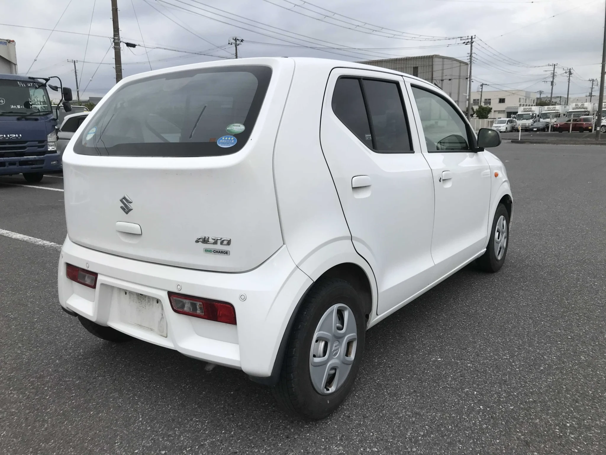Rear perspective view of the white 2019 Suzuki Alto showing its vertical clear-lens taillights, clean tailgate, and flush-fitted rear bumper parking sensors.